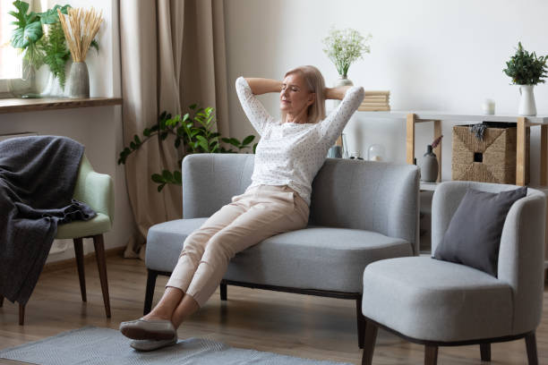 istock Attractive elderly woman resting on couch putting hands behind head 1191287524