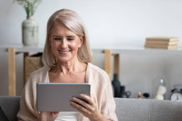 istock Attractive 60s woman sitting on couch with tablet computer 1191287577