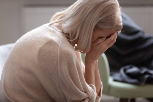istock Senior woman hides face with hands crying seated on couch 1191287582