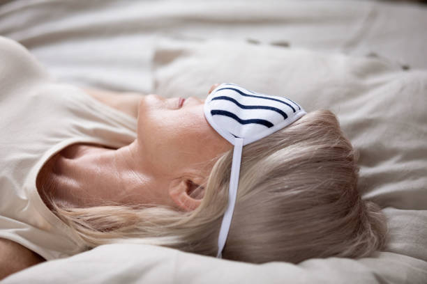 primer plano 50s mujer madura usando máscara para dormir acostado en la cama - women middle aging process covering fotografías e imágenes de stock