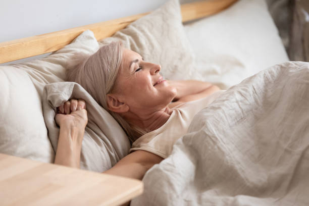 mulher de meia idade satisfeita que encontra-se na cama aprecia o amanhecer - lying down bedroom adult beautiful - fotografias e filmes do acervo