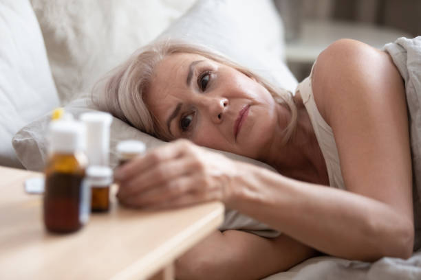 Old woman lying in bed looking at heap of pills Close up unhealthy old woman lying in bed woke up in morning looking at heap bottle of pills on bedside table feels cheerless, tablets to reduce menopause symptoms, chronic disease treatments concept sleeping pill stock pictures, royalty-free photos & images