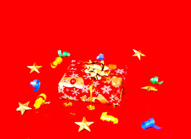 istock Christmas gift in festive packaging on red background with confetti. Copy space 1191299181
