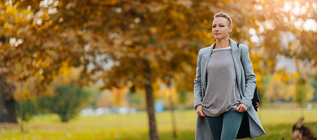 Woman with short hair wearing grey coat walking at park in autumn