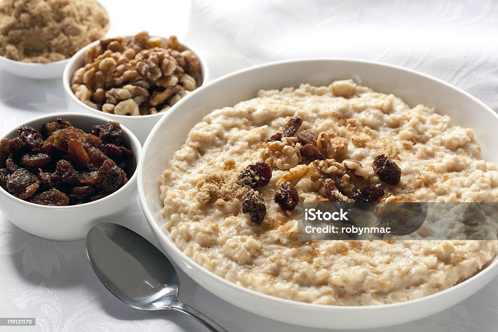 Bowls of oatmeal sitting on white detailed tablecloth Oatmeal with raisins, walnuts, and brown sugar.  Delicious traditional porridge. Raisin Stock Photo