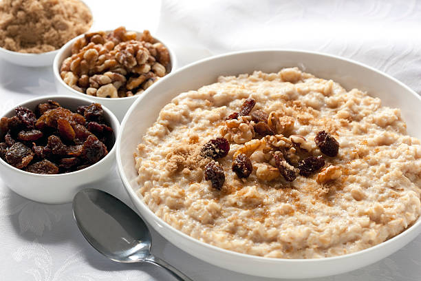 Bowls of oatmeal sitting on white detailed tablecloth Oatmeal with raisins, walnuts, and brown sugar.  Delicious traditional porridge. raisin stock pictures, royalty-free photos & images