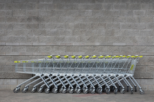 Many empty shopping trolleys with yellow handle standing in a row in the centre of photo at gray brick background of supermarket with copyspace