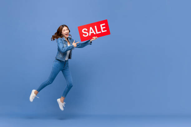 excited asian woman jumping with red sale sign - great discounts imagens e fotografias de stock