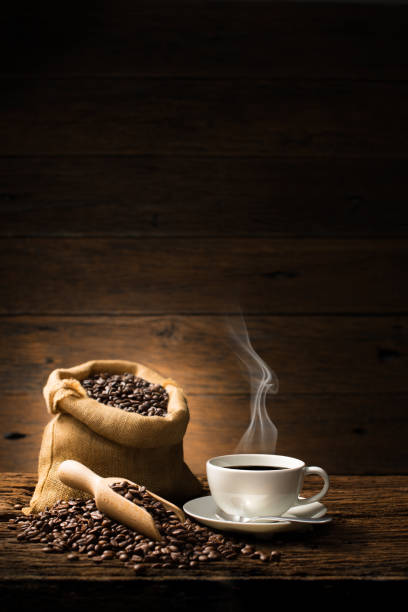 tazza di caffè con fumo e chicchi di caffè su vecchio sfondo di legno - cup of coffee beans foto e immagini stock