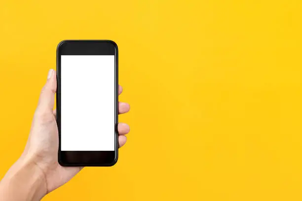 Hand holding empty screen mobile phone isolated on yellow background with copy space