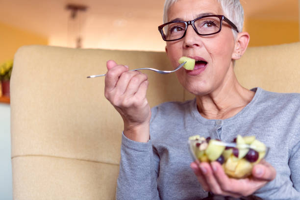istock Woman sitting on couch eating fruit salad 1191329090