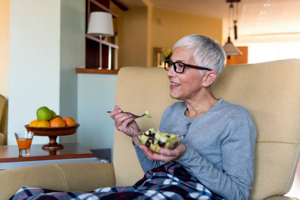 istock Woman sitting on couch eating fruit salad 1191329110
