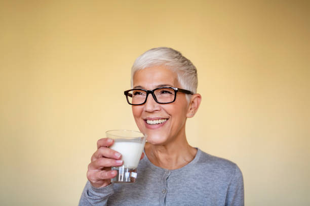 allegra donna matura che si gode in un bicchiere di latte a casa. - mature women beautiful senior women menopause foto e immagini stock