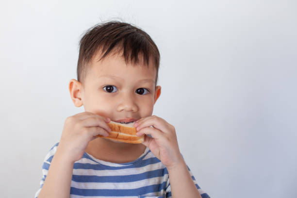 niño asiático comiendo pan antes de ir a la escuela - eating child cracker asia fotografías e imágenes de stock