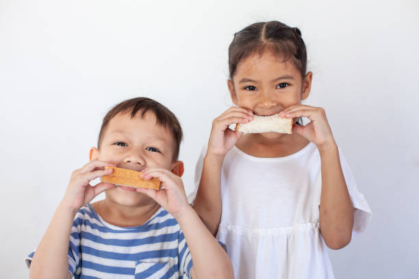 niño y niña asiáticos comiendo pan juntos antes de ir a la escuela - eating child cracker asia fotografías e imágenes de stock