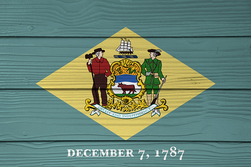 Delaware flag color painted on Fiber cement sheet wall background, the states of America, yellow diamond shape on green with coat of arms of the state and the date December 7, 1787.