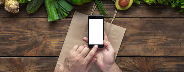 istock Male hands holding smartphone with blank screen for your text message or design with green green vegetables. Food ordering through mobile cell phone application concept 1191358441