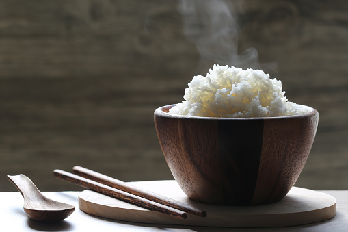 cooked rice in wood bowl with smoke rising on dark background