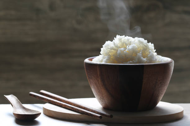 cooked rice in wood bowl with smoke rising on dark background cooked rice in wood bowl with smoke rising on dark background boiled stock pictures, royalty-free photos & images