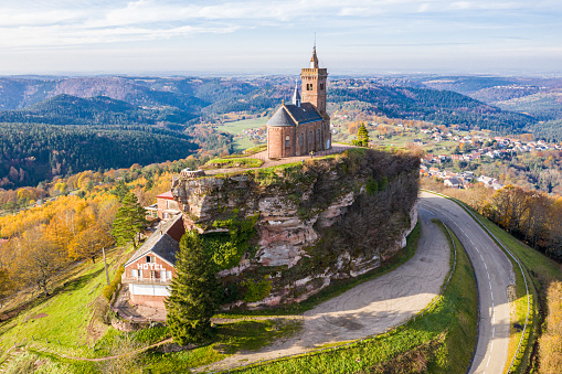 Beautiful autumn aerial view of St. Leon chapel dedicated to Pope Leo IX atop of Rocher de Dabo or Rock of Dabo, red sandstone rock butte, and Moselle-Vosges mountains and valleys. Lorraine, France.