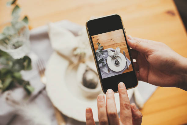 istock Hand holding phone and taking photo of stylish Easter flat lay table setting with egg in easter bunny napkin. Modern Easter table decorations workshop. Photo for social media 1191363532
