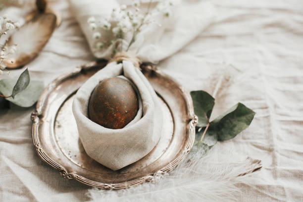 istock Rustic Easter table decorations. Modern natural dyed egg on napkin with bunny ears, flowers on vintage plate.Stylish Easter brunch table setting with egg in easter bunny napkin. 1191363656