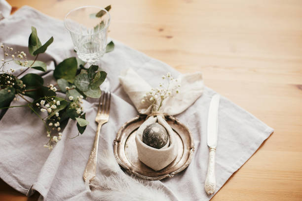 istock Easter table decorations. Modern natural dyed gray egg on napkin with bunny ears, flowers on vintage plate and cutlery. Stylish Easter brunch table setting with egg in easter bunny napkin. 1191363806