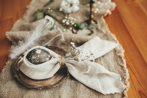 istock Stylish Easter brunch table setting with egg in easter bunny napkin. Modern natural dyed gray egg on napkin with bunny ears, flowers on vintage plate. Rustic Easter table decorations 1191363953