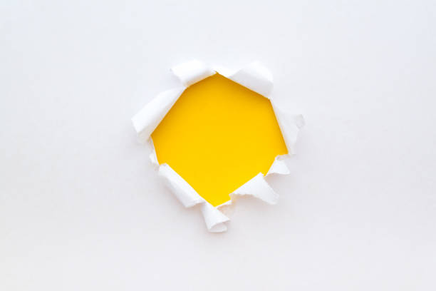 istock A round hole in white paper with torn edges with a bright yellow color paper background inside. 1191365744