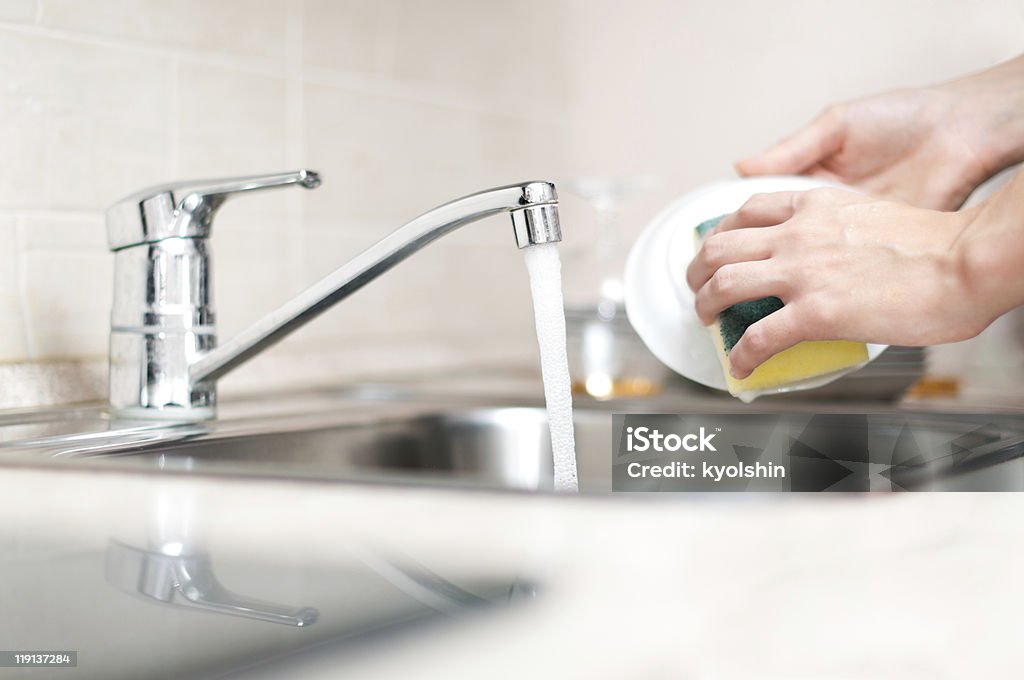 Hands holding and washing a bowl in the kitchen sink woman hand holding yellow sponge and washing saucer with washed dishes in background Adult Stock Photo