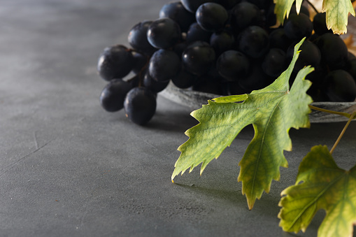 Wine grapes in a glass bowl and grape leaves on the table. Dark background.