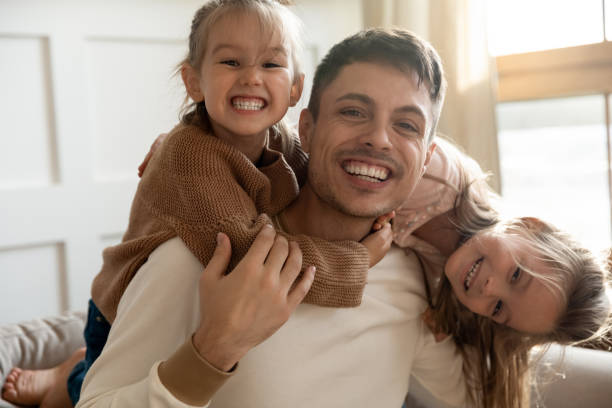 istock Funny father and two kids daughters embracing looking at camera 1191377518
