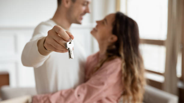 Happy couple hugging holding keys buy new apartment concept, closeup Happy couple hugging holding keys rent buy new apartment, young first time home buyers renters owners moving in own house, mortgage loan, property ownership concept, close up view, focus on keychain happy family with key of their new house stock pictures, royalty-free photos & images