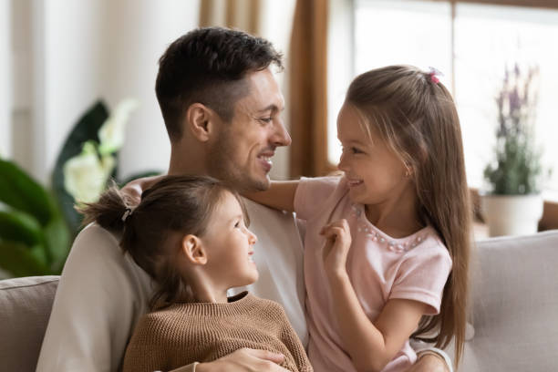 istock Affectionate father hugging little children daughters bonding sitting on sofa 1191377771