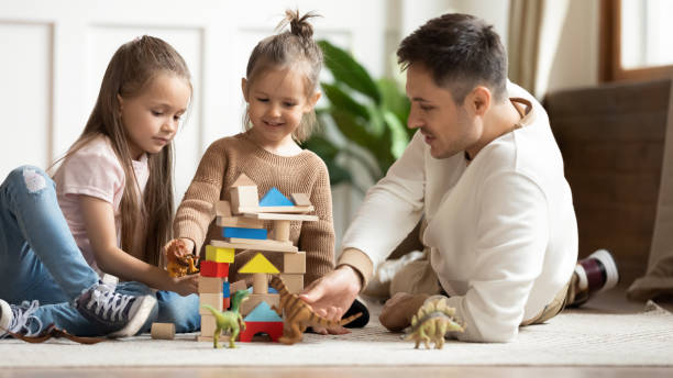 Caring young dad and small daughters playing together at home
