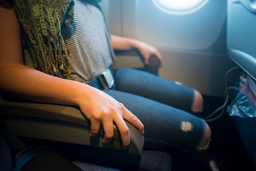 Anonymous scared young woman gripping onto the air plane arm rest in fear as she is travelling on an air plane during turbulence.