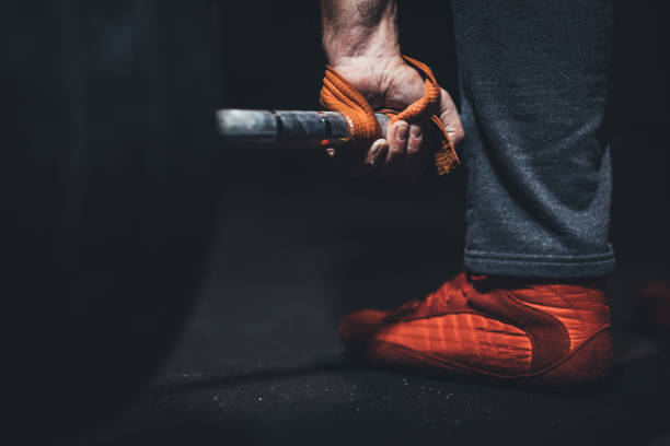 One man, body builder sitting alone in dark gym, training with barbell.