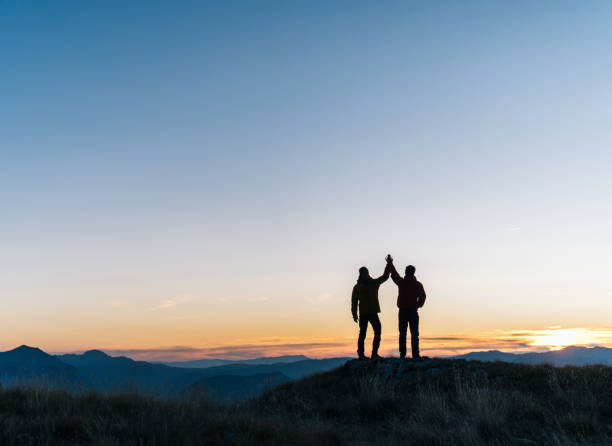 Hikers relaxes above mountain valley at sunrise They high-five each other male friendship stock pictures, royalty-free photos & images