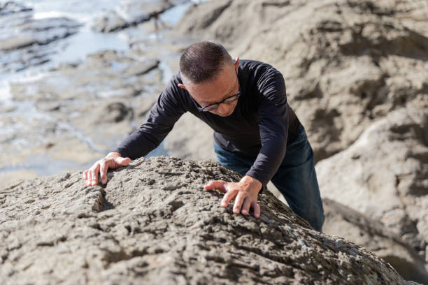 Young man aims to reach the top by climbing the cliffs in the sea at sunset. He believes that hard work is necessary for success.