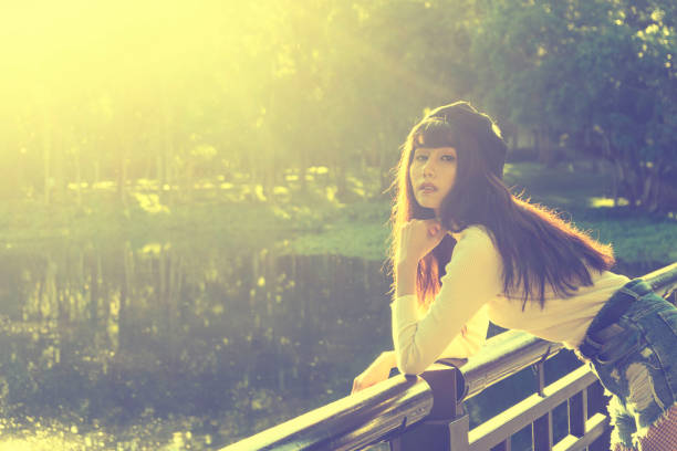 Beautiful soft portrait of asian woman standing on the bridge with lake over morning sunlight sky background
