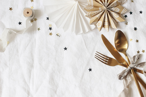 Christmas, New Year composition. Decorative table setting. Paper stars, golden cutlery and confetti stars on white linen background. Celebration, birthday party concept,flat lay, top view, copy space