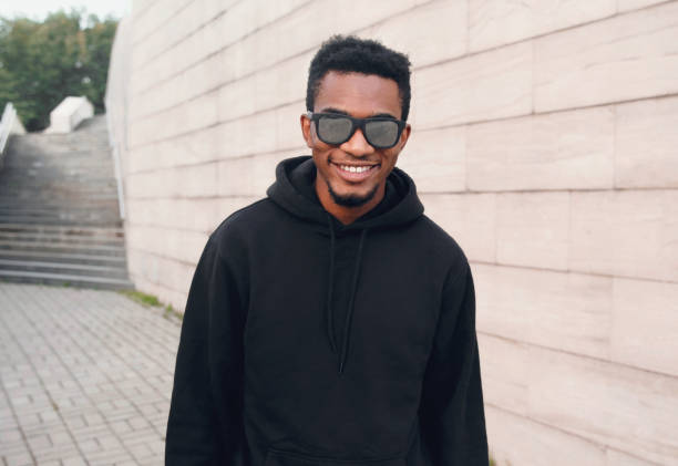 Portrait happy young smiling african man wearing black hoodie, sunglasses on city street stock photo