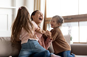 Small kids daughters tickling playing with happy mum on sofa