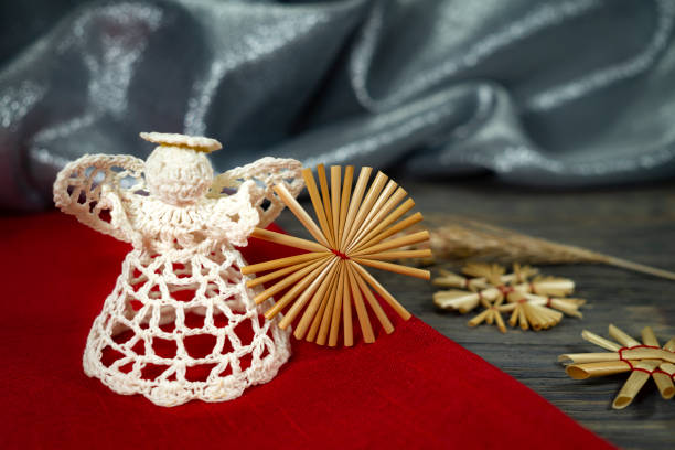 Rustic Christmas still life with handcrafted straw ornaments, a crocheted angel, matching red fabric on a wooden background, eco friendly Christmas toys concept