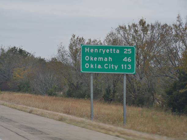 mittelweite aufnahme eines straßenschildes mit entfernungen zu henryetta, okema und oklahoma city. - oklahoma sign road sign sky stock-fotos und bilder