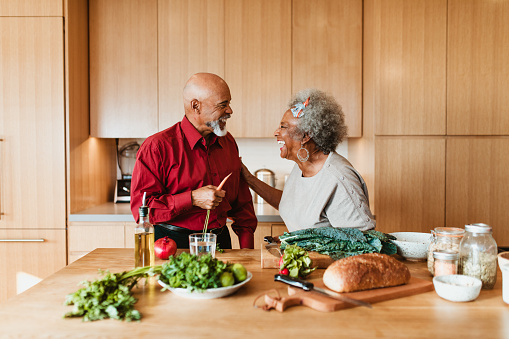 Cheerful senior couple preparing meal in kitchen at home. Retired man and woman are laughing while looking at each other. They are spending leisure time.