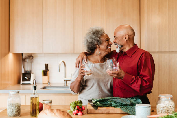 Smiling senior couple holding alcoholic drink Happy man and woman looking at each other at kitchen island. Senior couple is holding alcoholic drink in kitchen. They are standing with arm around. brunch photos stock pictures, royalty-free photos & images