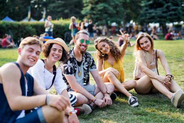 Group of young friends sitting on ground at summer festival. Group of cheerful young friends sitting on ground at summer festival, looking at camera. music festival camping summer vacations stock pictures, royalty-free photos & images