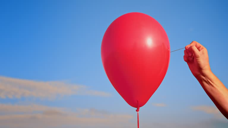 SLO MO LD Hand popping a red balloon with a needle