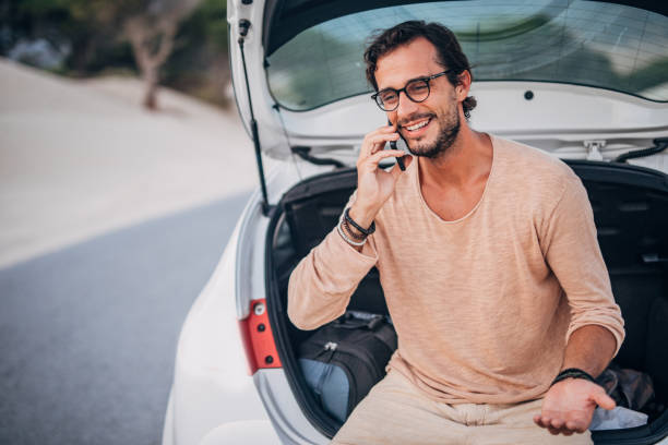 istock Guy sitting on car trunk and talking on mobile 1191403000